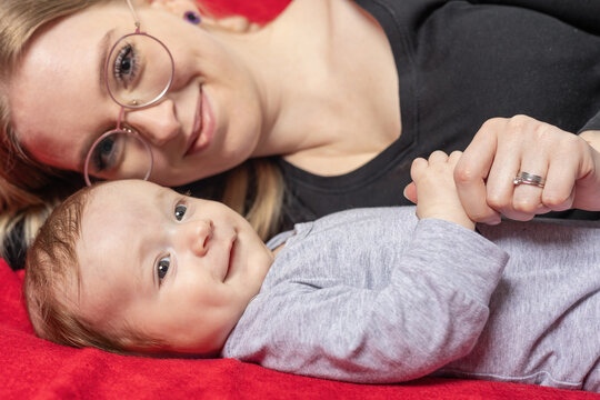 Smiling mother is lying with her newborn baby boy looking at the camera. Horizontally. 