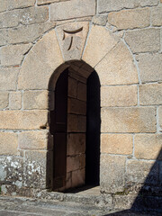 Puerta con un arco y una cruz templaria arriba en una fachada de piedra antigua, verano de 2021, pueblo de León, España.