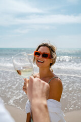 Couple shares a cheerful toast with glasses of white wine on the beach