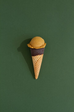 Scoop of pistachio ice cream in a cone on green backdrop