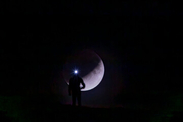 A stunning silhouette of a lone individual wearing a headlamp, standing before a backdrop of the crescent moon in a dark, serene night sky
