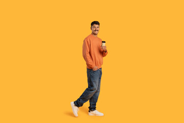 Casual man walking with coffee on yellow