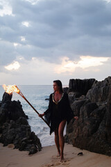 Mysterious woman on the beach at dusk and holding a flaming torch