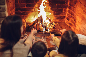 Happy young family parents with two small kids gathering around brick fireplace in cozy and warm...