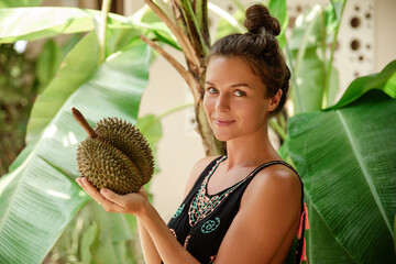 Happy woman holds a spiky durian fruit in a lush tropical garden