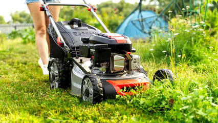 A girl with a lawn mower mows green grass