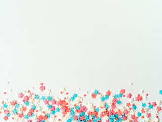 Festive border frame of colorful pastel sprinkles on white background, copy space top. Sugar sprinkle dots and stars, decoration for cake and bakery. Top view or flat lay