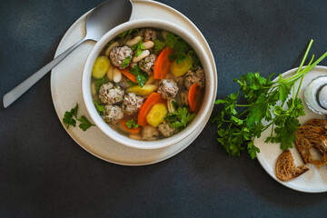 White bean beef meatball soup with  seasonal vegetables on grey background, directly abiove