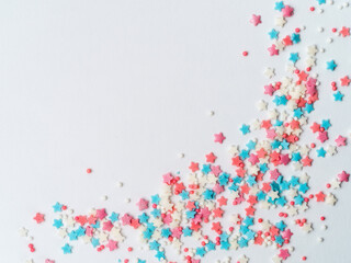 Festive border frame of colorful pastel sprinkles on white background with copy space one edge. Sugar sprinkle dots and stars, decoration for cake and bakery. Top view or flat lay