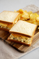Homemade Egg Salad Sandwich with Potato Chips on a wooden board, side view. - 785668039