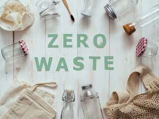 Zero waste concept. Textile eco bags, glass jars and bamboo toothbrush on white wooden background with Zero Waste green paper text in center. Eco friendly and reuse concept. Top view or flat lay