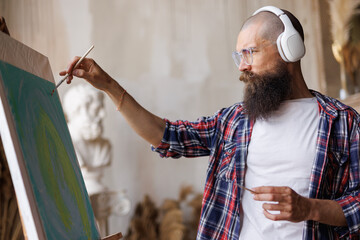 Moving paint brush artist works on abstract oil painting in creative modern studio. Guy with...