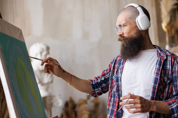 Moving paint brush artist works on abstract oil painting in creative modern studio. Guy with...