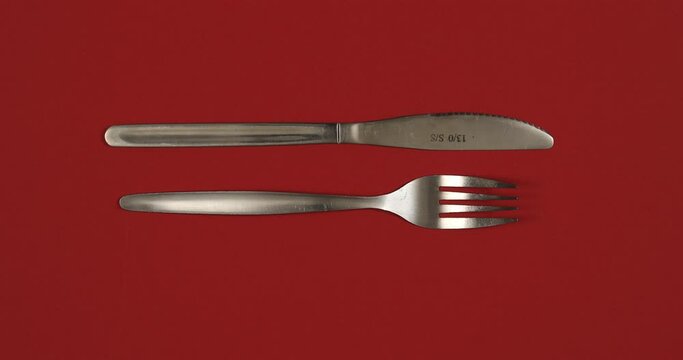 Cutlery stop motion animation. Different kinds of knives and forks changing on red background. 4K top view shot.