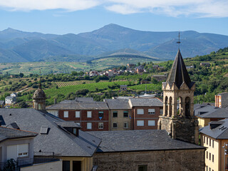 Vista del campanario de la Basílica de la Virgen de la Encina con el fondo de un paisaje de tejados y montañas verdes con cielo azul en verano de 2021 en León ,España.