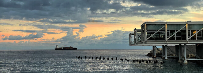 Container Schiff am Horizont gesehen vom Hafen in Limassol, Zypern bei Sonnenuntergang  - obrazy, fototapety, plakaty