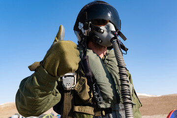 A man in a military, in pilot suit uniform is giving a thumbs up sign. He is wearing a pilot mask