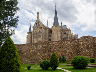 Vistas de la fachada del Palacio de Gaudí Astorga, con una muralla de de piedra y cúpulas en las torres, en un paisaje con jardín verde, césped y arbustos , verano de 2021 en Ponferrada, España