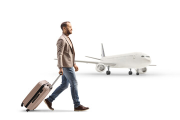 Full length profile shot of a man walking and pulling a suitcase near an airplane