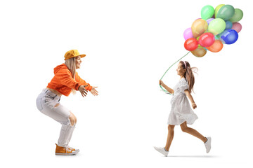 Full length profile shot of a girl with balloons running towards a young female with arms wide open