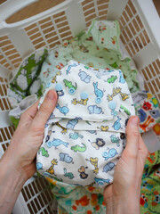 Female hands holding a cloth diaper inside a laundry basket full of clean colorful cloth bamboo...