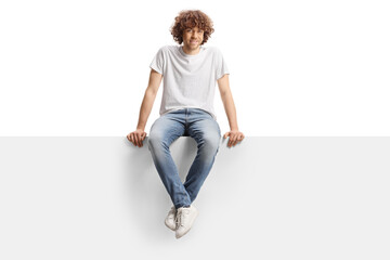 Cute guy with curly hair sitting on a blank panel