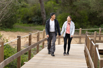 A man and woman are walking on a wooden bridge