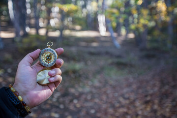 A person holding a compass in a forest. The forest is full of trees and leaves. trip, travel and discovery concept