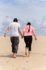 A couple is walking on a sandy beach, holding hands
