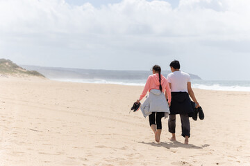 A couple walking on a beach with a man carrying a camera