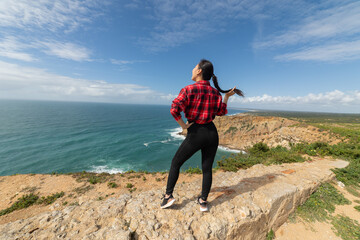 A woman stands on a rocky cliff overlooking the ocean