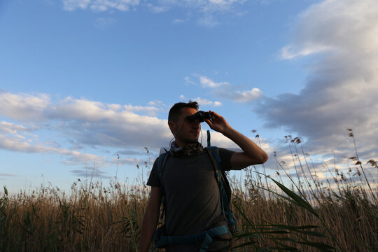 Young man looking at the horizon with binoculars outdoor. man using binoculars in sunset nature