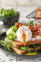 Toasts sandwich with poached egg, cucumber, arugula, bacon and cream cheese on printed tile kitchen background for healthy breakfast, close up