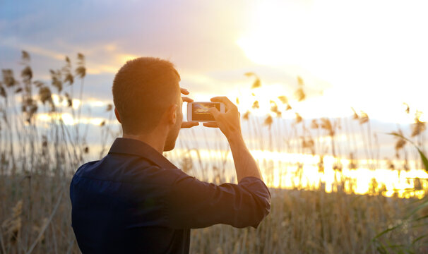A man takes a photo of nature at sunset with his mobile phone