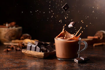 Pieces of dark chocolate fall into a glass of cocoa drink creating a beautiful splash.