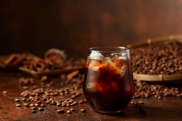 Black iced coffee with coffee beans on a brown vintage table.