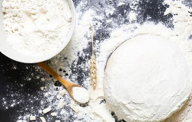 Raw dough flour and ears of wheat on black background top view Home baking concept