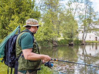 Senior fisherman holding a fishing rod with a spinning reel, getting ready to catch a fish. Fishing equipment and skills concepts.