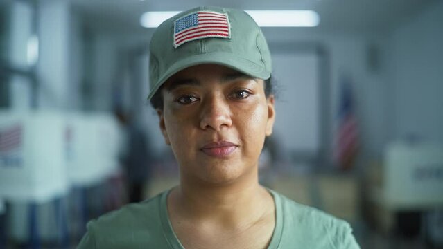 Portrait of female soldier, United States of America elections voter. Woman in camouflage uniform stands in polling station and looks at camera. Background with voting booths. Concept of civic duty.