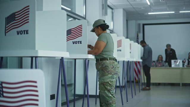 American female soldier stands at voting booth in polling station office. National Election Day in United States. Political races of US presidential candidates. Concept of civic duty and patriotism.