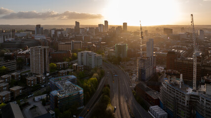 The sun pierces the morning sky, casting a serene glow over Leeds, emphasizing the construction and architectural landscape of the busy city centre from a drone's view