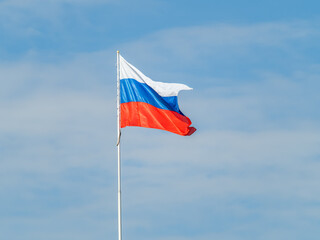 Russian tricolor flag waving in the wind against a blue sky.