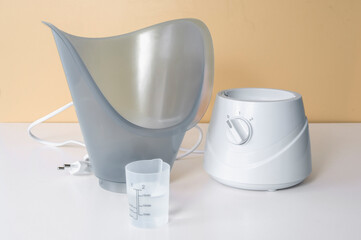 Facial steamer with water containers On a white table and beige background