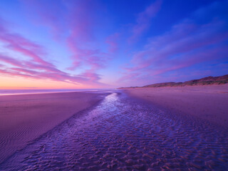 Seascape during sunrise. Bright clouds on the sky. Lines of sand on the seashore. Bright sky during...
