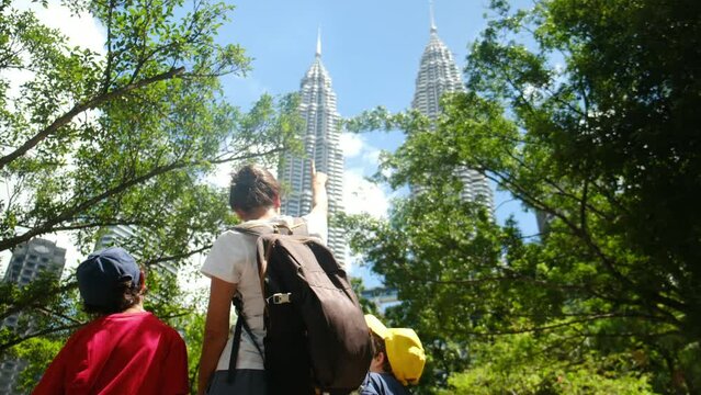 Fearless single mother travels with her 5 and 7-year-old children, exploring Kuala Lumpur's Petronas Towers and Southeast Asian cityscape on a summer adventure, proving that family travel knows no bou