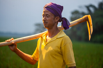 indian farm worker standing in the field with a shovel or grub hoe.