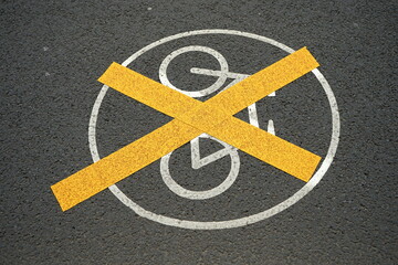 Gelb durchkreuzte weiße Markierung mit weißem aufgemaltem Verkehrszeichen auf dem grauen Asphalt...