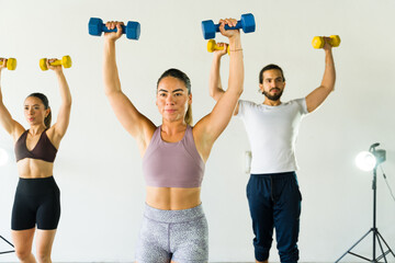 Group of Hispanic people training in a gym class lifting dumbbells