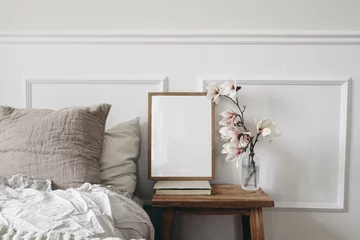 Foto op Plexiglas Blank wooden picture frame mockup on old book. Wooden night stand with fluted glass vase. Blooming magnolia tree branches. Scandinavian interior. Elegant bedroom. White wall background, stucco decor. © tabitazn