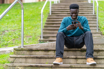 A young man is sitting on a set of stairs with his cell phone in his hand